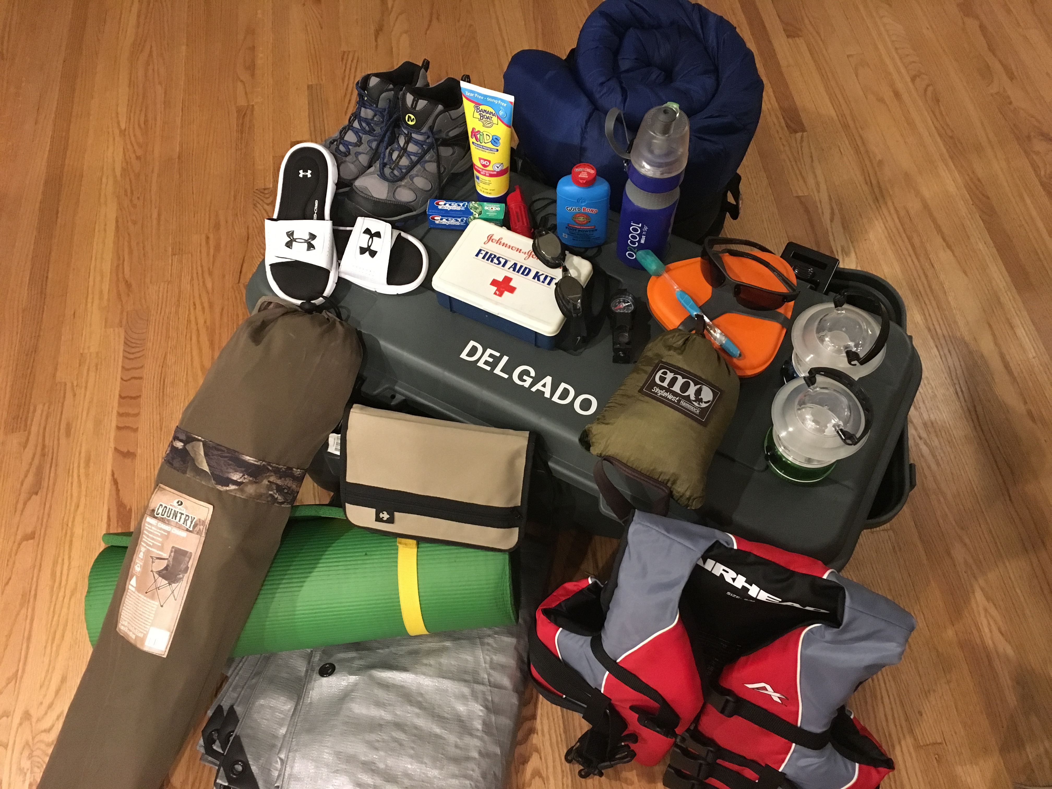 Hiking boots, sunscreen bottle, toothpaste, whistle, first aid kit, goggles, compass, mess kit, toothbrush, hammock, lanterns, sleeping bag, foot powder bottle, flip flops, nylon book cover, camp chair, sleeping pad, tarp, life preserver, foot locker.
