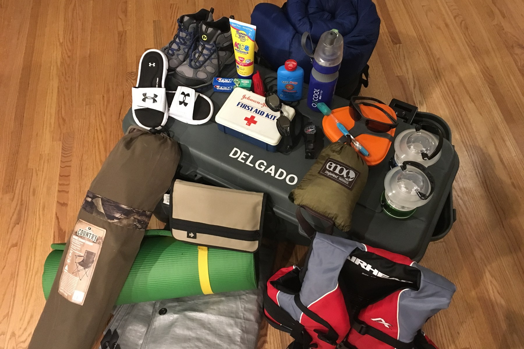 Hiking boots, sunscreen bottle, toothpaste, whistle, first aid kit, goggles, compass, mess kit, toothbrush, hammock, lanterns, sleeping bag, foot powder bottle, flip flops, nylon book cover, camp chair, sleeping pad, tarp, life preserver, foot locker.